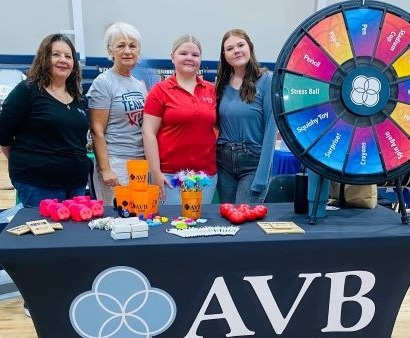 Four women standing around a table with a prize wheel and promo items for a hiring event. 